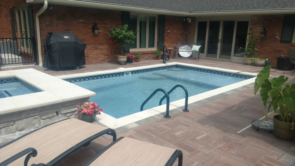 Rectangular swimming pool with adjacent raised spa, white pool coping and brown paver patio in Alton, Illinois.